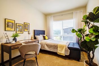 A bedroom with a bed, desk, chair, and a potted plant.