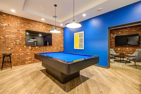 A pool table in a room with a brick wall and a television.