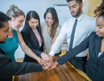 A group of professionals stacking their hands together in a show of unity.