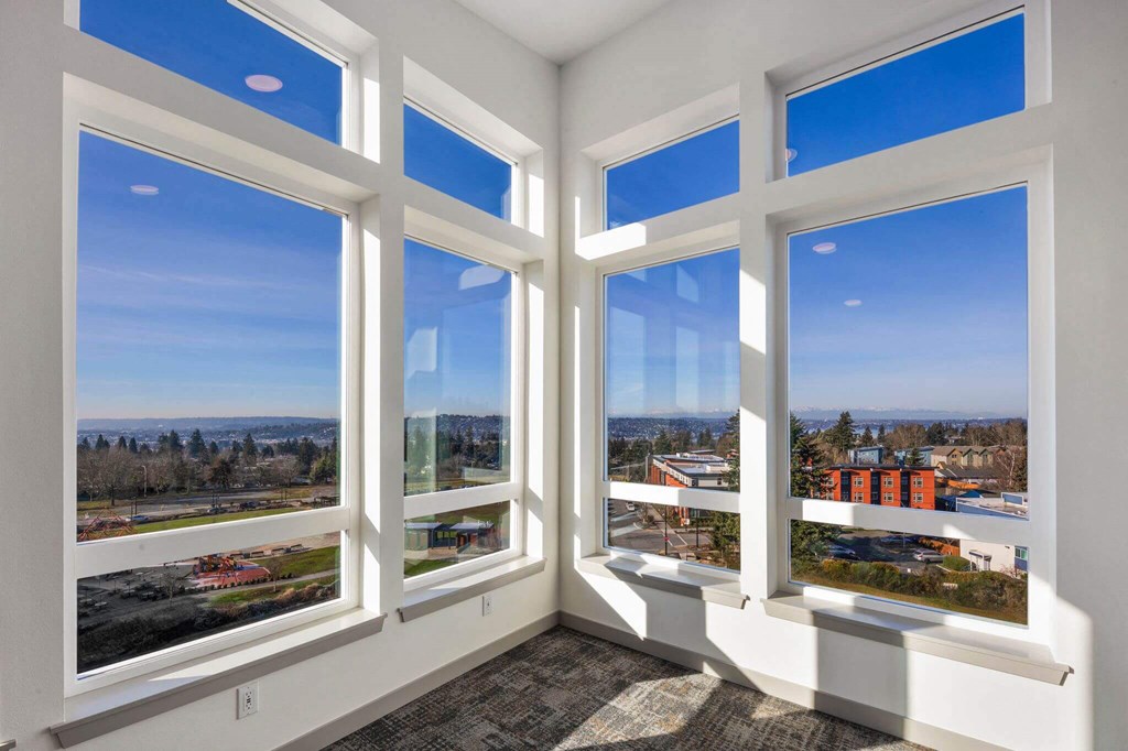 A room with four large windows overlooking a parking lot and buildings.