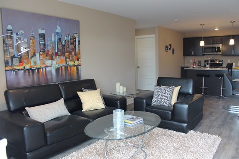 A living room with black leather furniture and a cityscape painting on the wall.