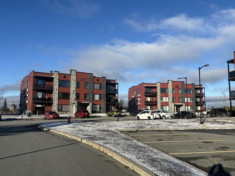 A parking lot in front of a red and grey apartment building.