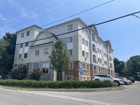 A large white building with a grey roof and a parking lot in front.