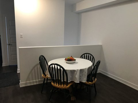 A table with a white cloth and a bowl of fruit on it is surrounded by four chairs.