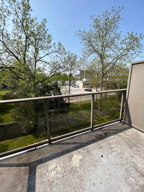 A balcony with a metal railing and a view of a parking lot and trees.