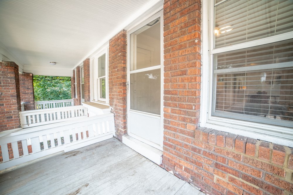 the front porch of a brick house with a white porch swing and a brick wall
