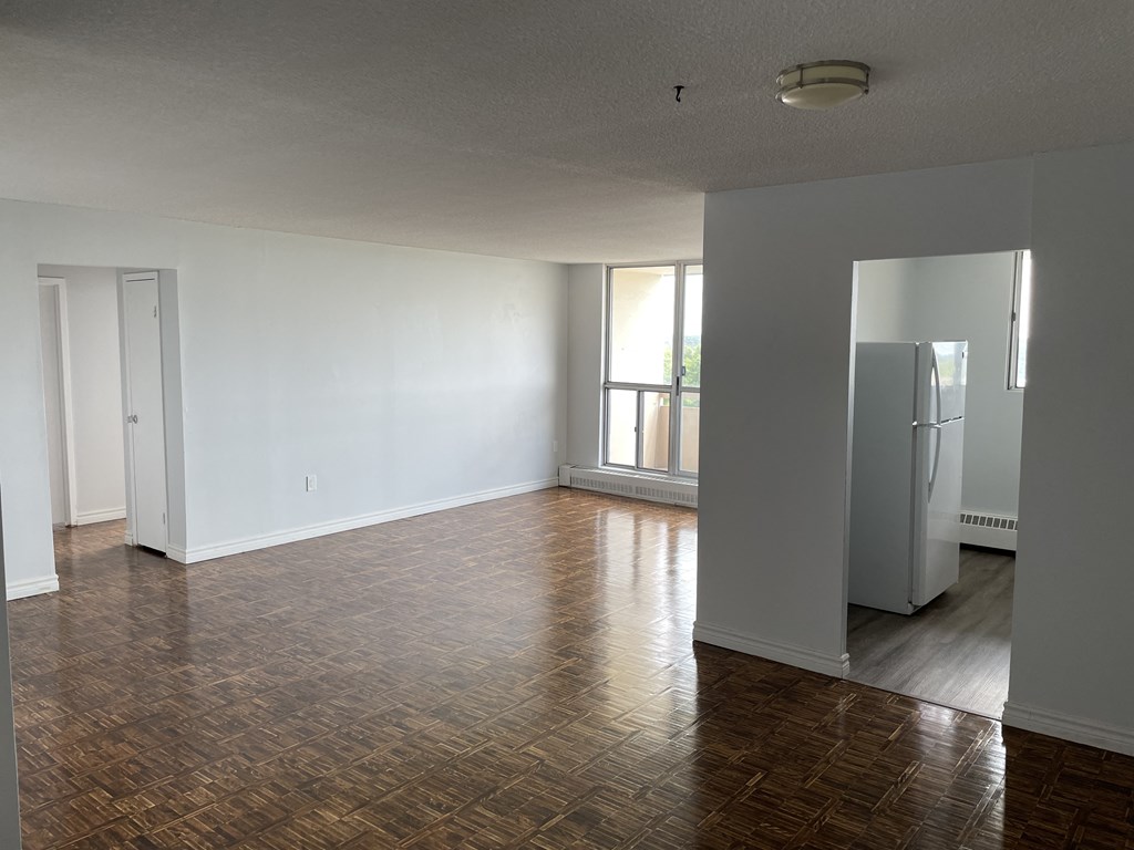 an empty living room with wood floors and a refrigerator