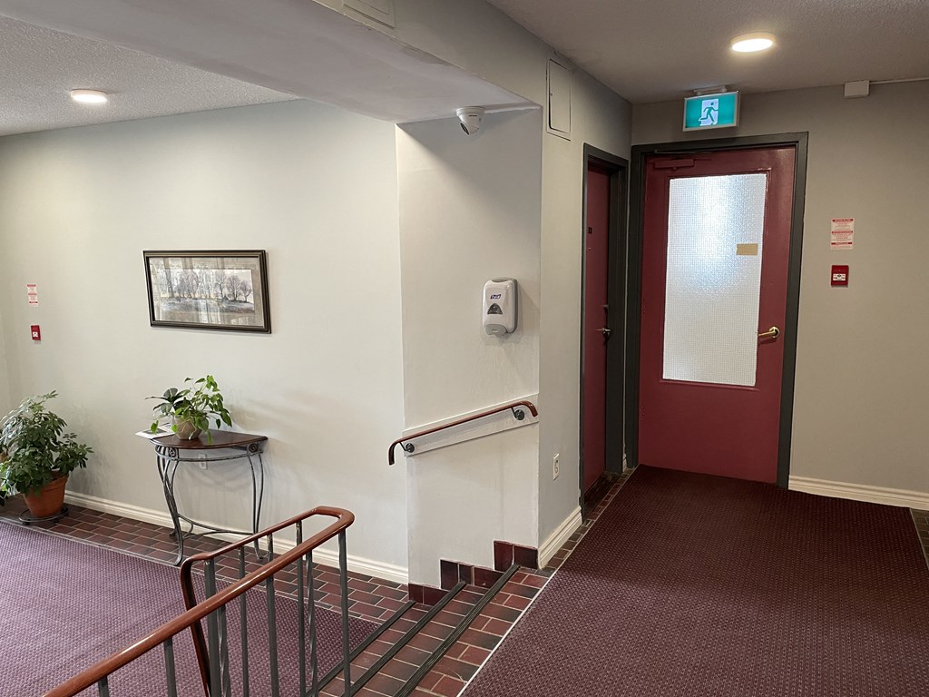 a hallway with a red door and a stairwell with a railing and a plant
