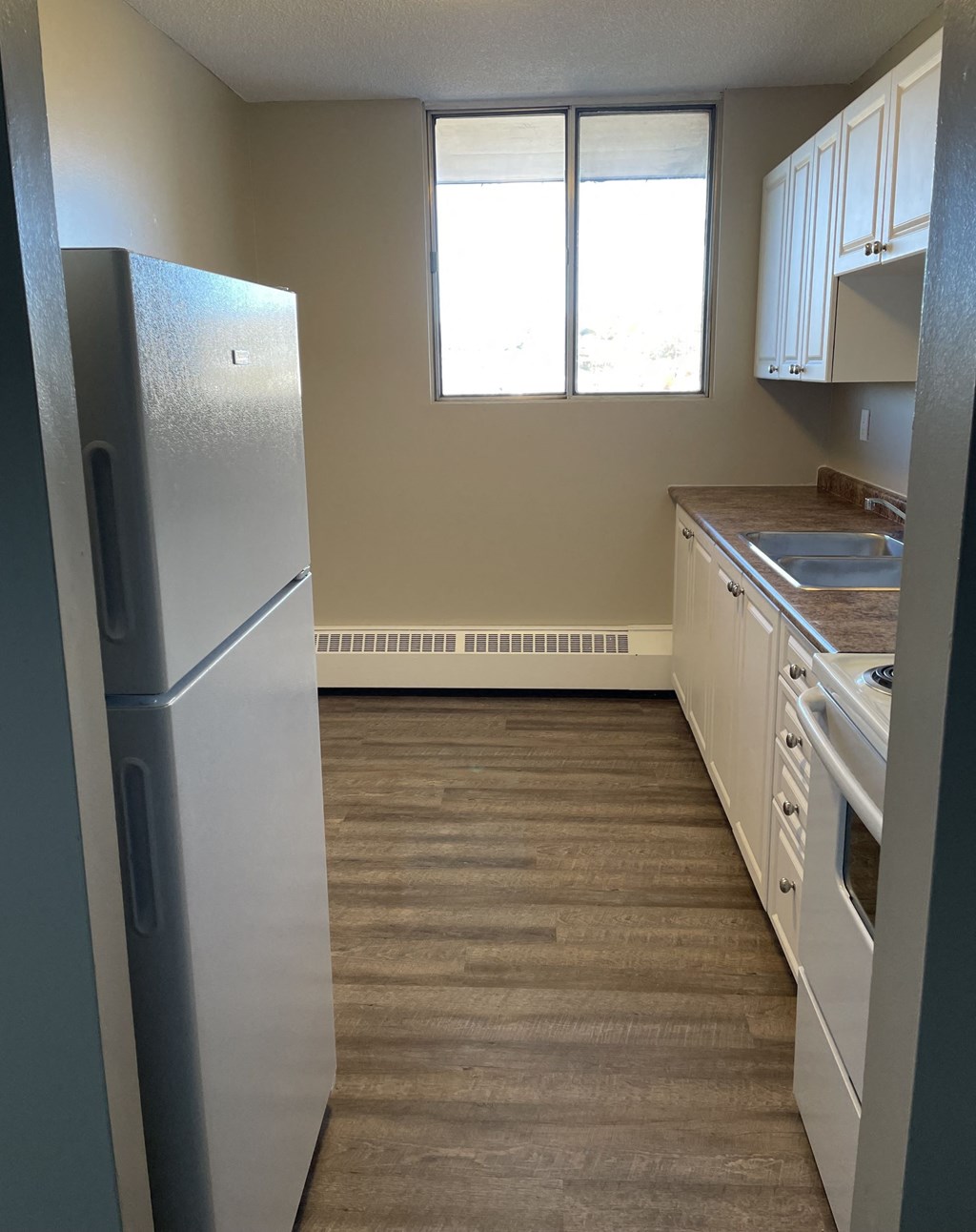 A kitchen with a refrigerator, cabinets, and a window.