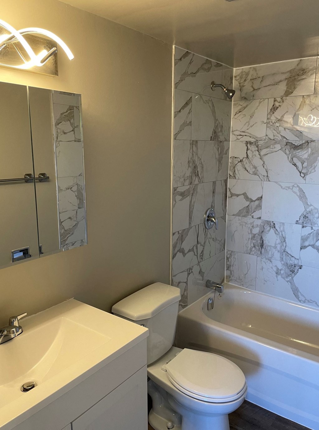 A white toilet sits next to a sink in a marble-tiled bathroom.