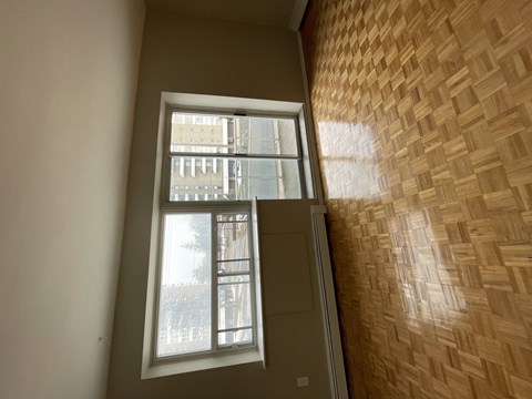 A window with a view of a building outside is in a room with a wooden wall.