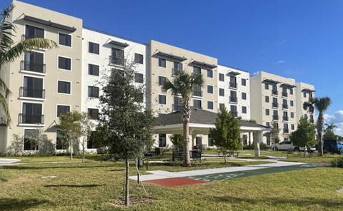 A row of white apartment buildings with balconies and trees in front.
