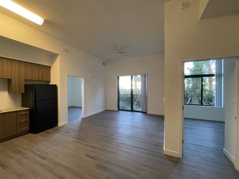 A spacious living room with a black refrigerator and wooden cabinets.