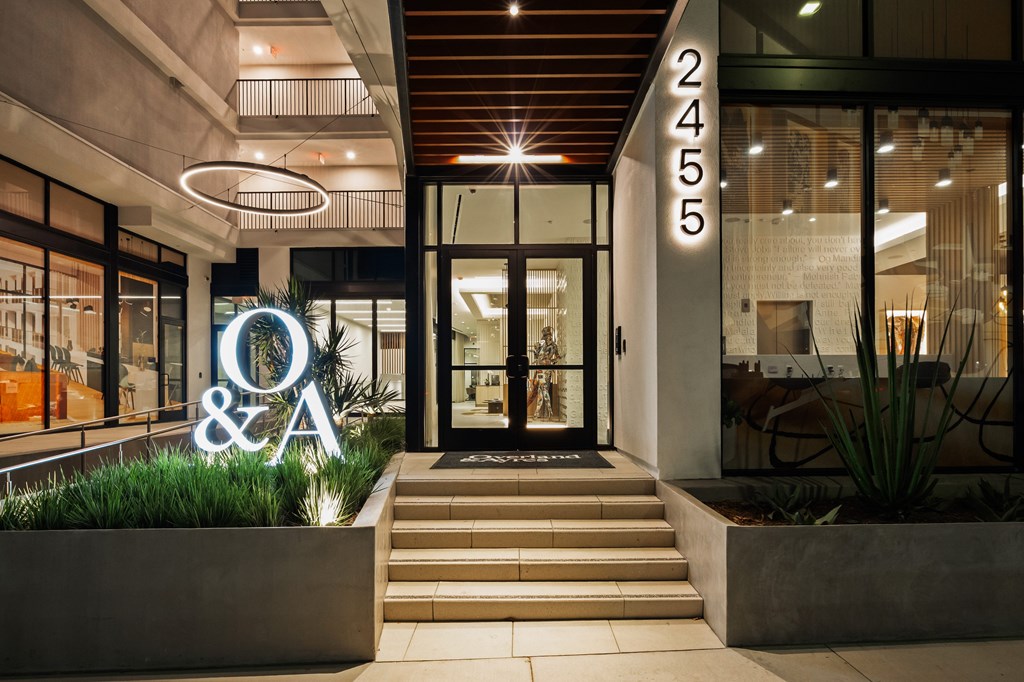 The image shows the entrance to a building with a glass door and a sign that reads "O&A" above a planter box.