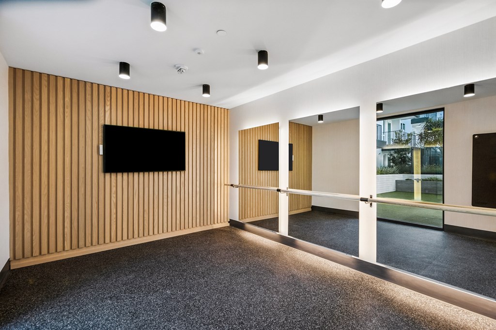 A room with a television on the wall and a window with a view of a building outside.