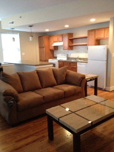 A brown couch sits in a kitchen with a white refrigerator.