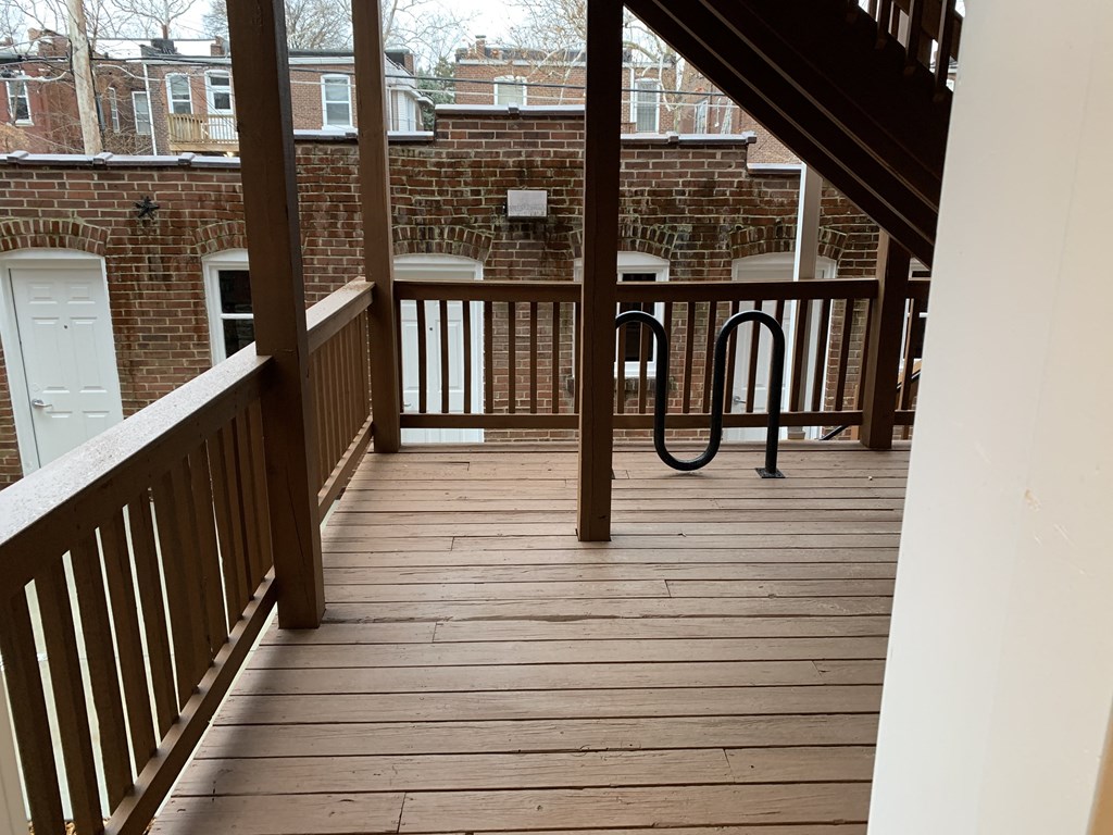 a balcony with a wooden floor and a brick building in the background