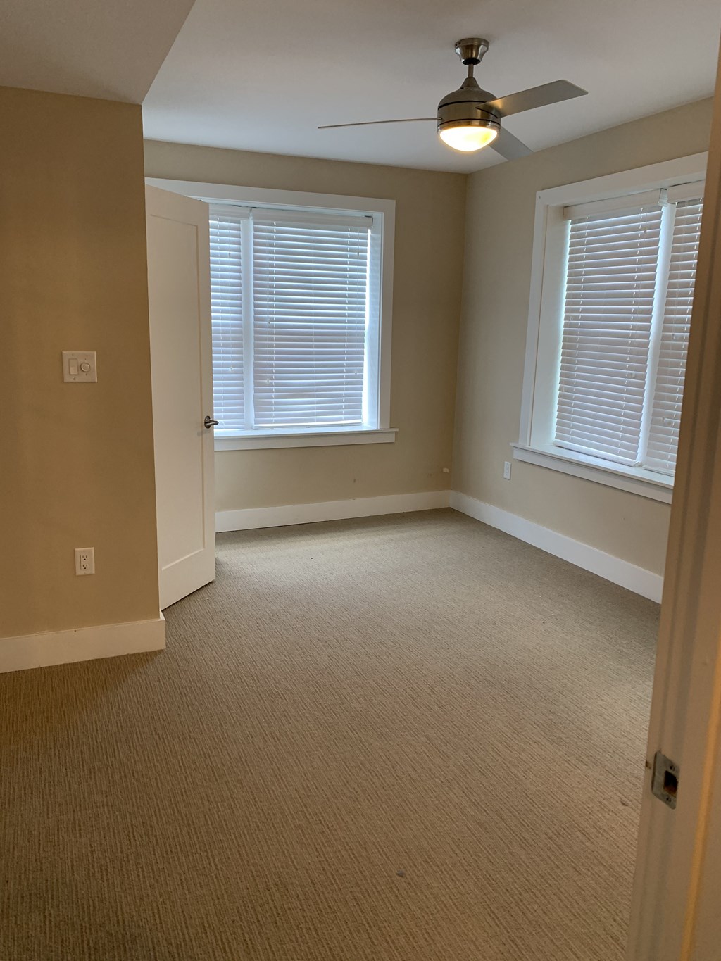 A room with a ceiling fan and two windows.