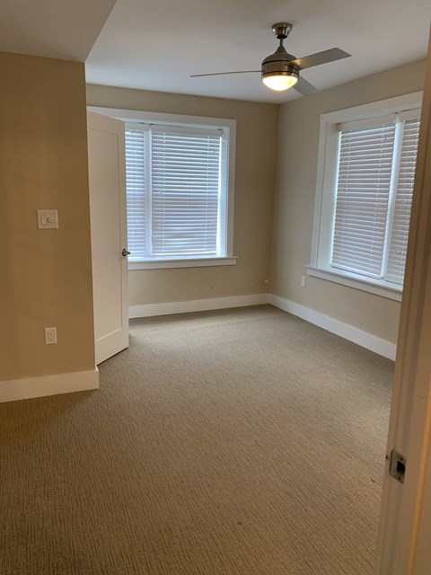A room with a ceiling fan and two windows.