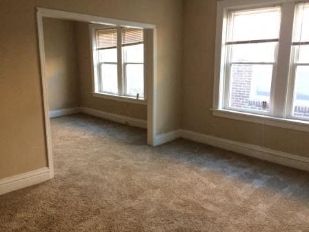 an empty room with two windows and a carpet