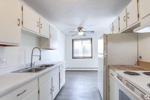 A white kitchen with a stove top oven and a window.