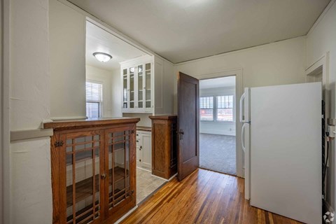 A white refrigerator is in a kitchen with wood floors and cabinets.