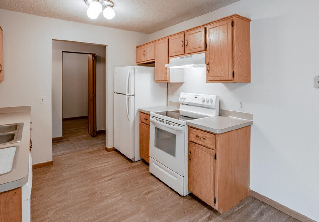 an empty kitchen with white appliances and wooden cabinets