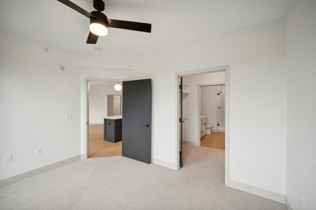 an empty living room with a ceiling fan and a door to a bathroom