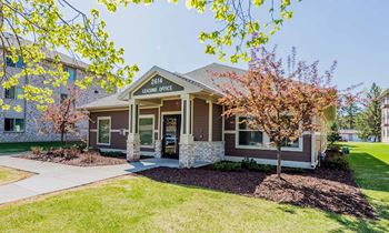 A house with a brown roof and a sign that says "3614 HOUSING OFFICE" is surrounded by trees and a mulched garden.