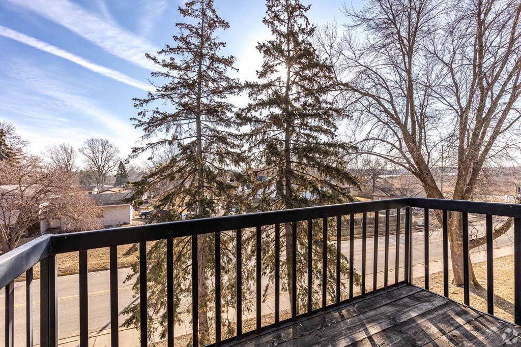 A balcony with a black 956 Place Apartments, Forest Lake, MNrailing and a view of a tree and a road.