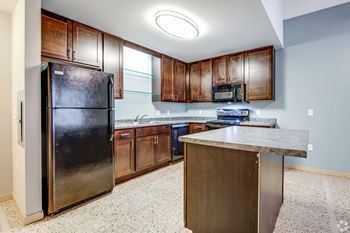 A kitchen with a black fridge, brown cabinets, and a granite countertop.