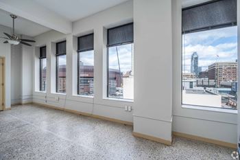 A room with a ceiling fan and large windows overlooking a cityscape.