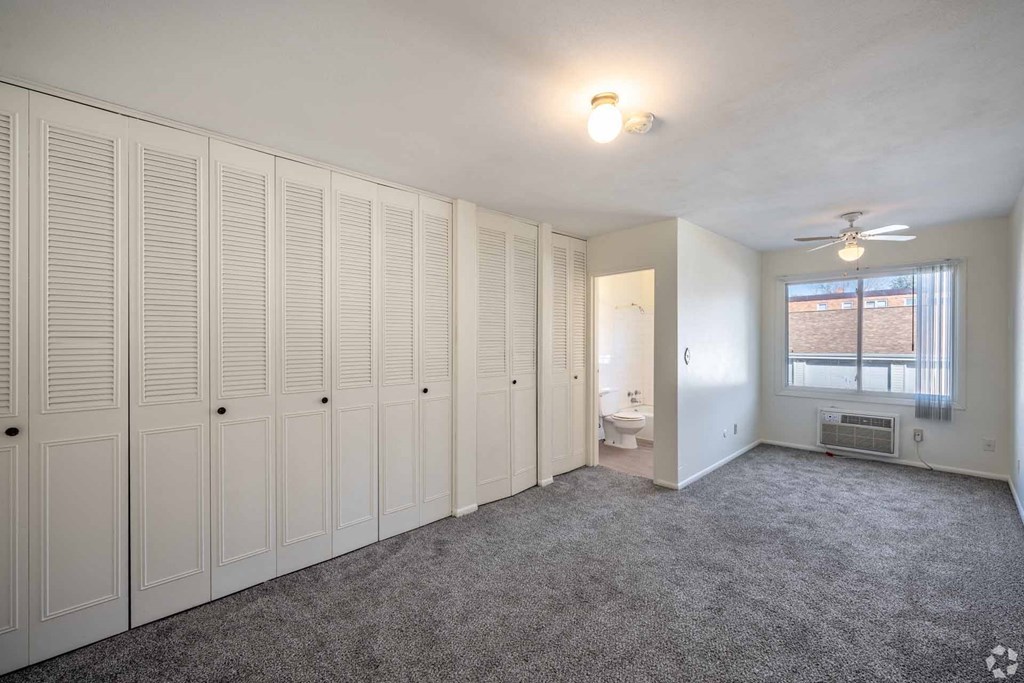 A room with white cupboards and a grey carpet.