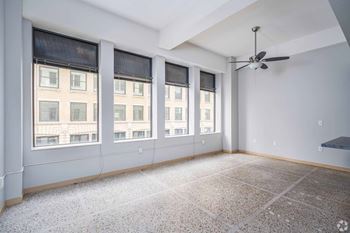 A room with a ceiling fan and large windows.