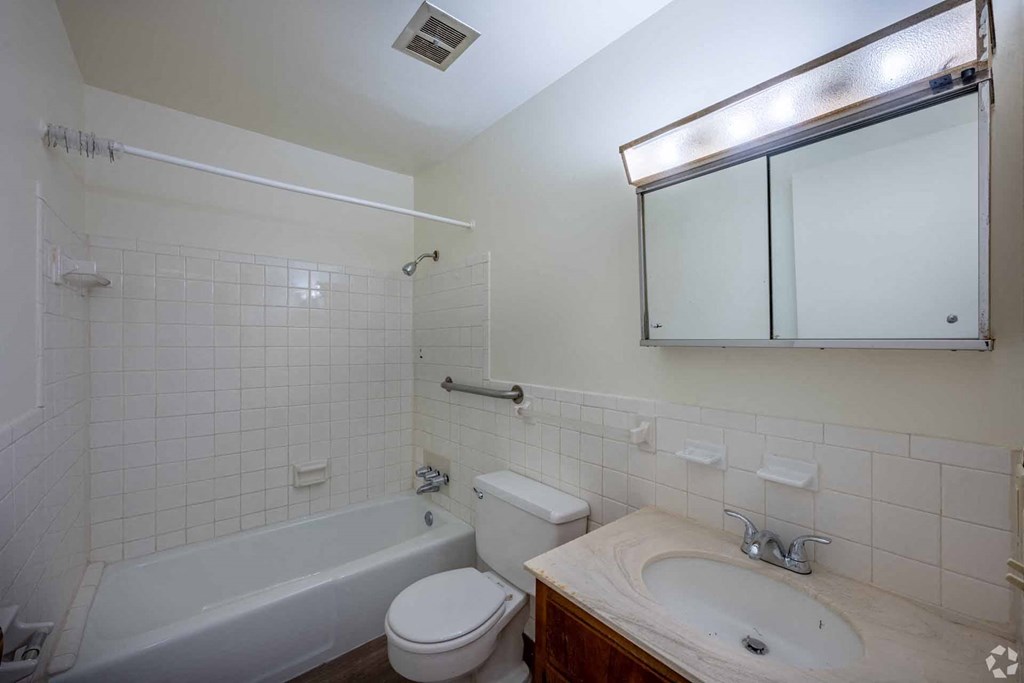A white tiled bathroom with a toilet, sink, and bathtub.