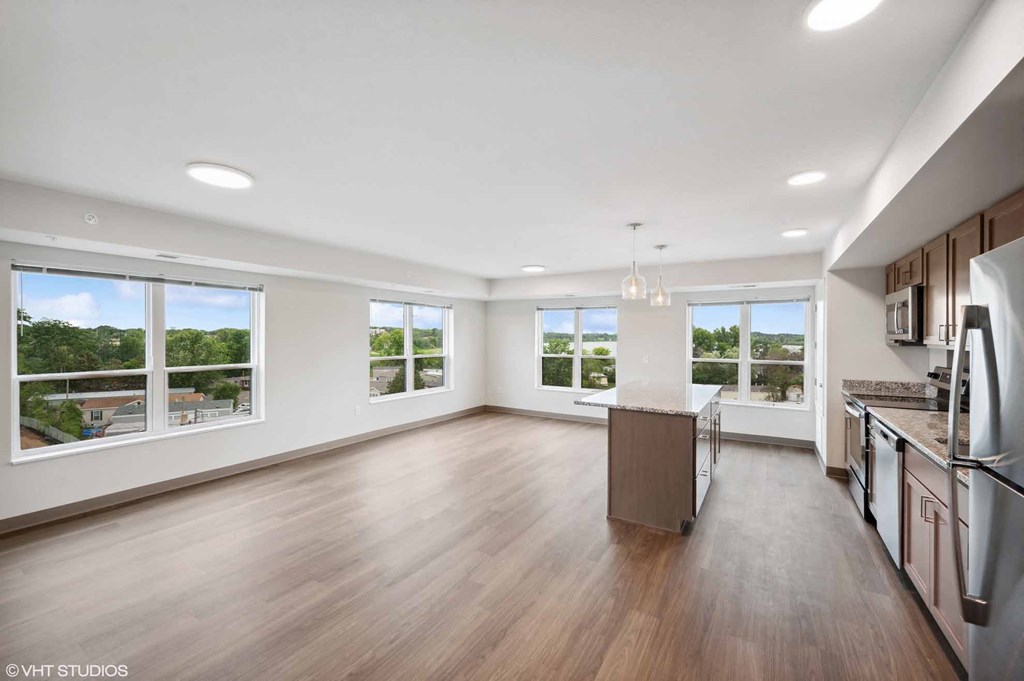 an empty living room with a kitchen and a large window