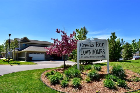 A sign for Creeks Run Townhomes stands in front of a house.