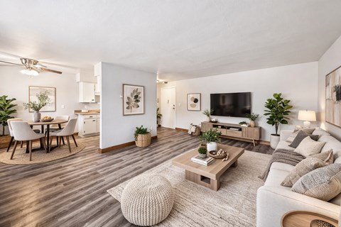 A modern living room with a white couch, a wooden coffee table, and a dining table with chairs.