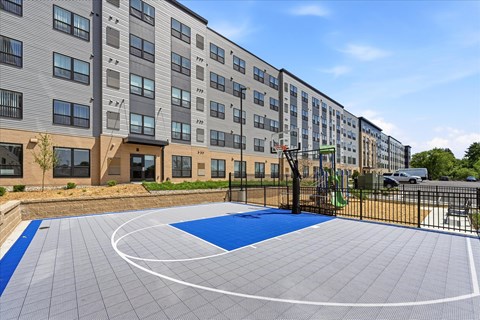 A basketball court is located in front of a multi-story apartment building.