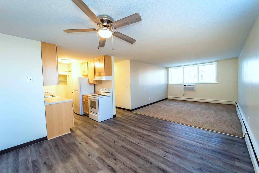A room with a ceiling fan and a kitchenette.