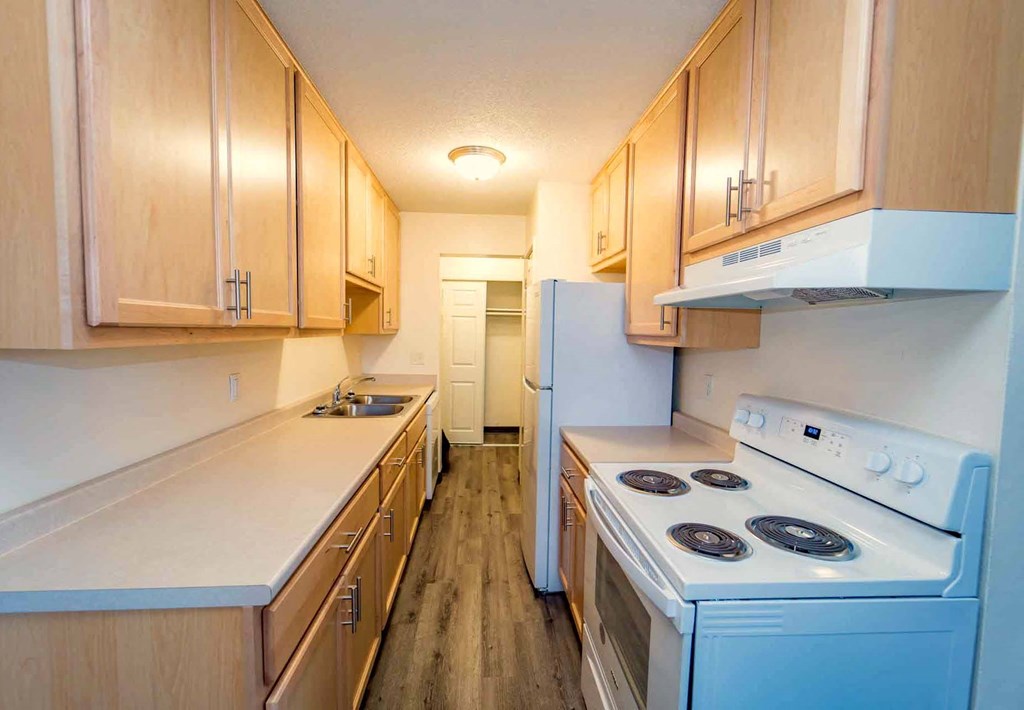 A kitchen with a white stove top oven and wooden cabinets.