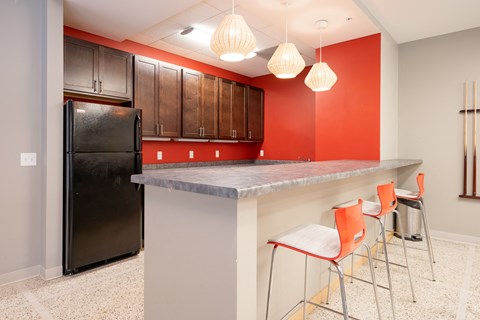 A kitchen with a black refrigerator and orange chairs.