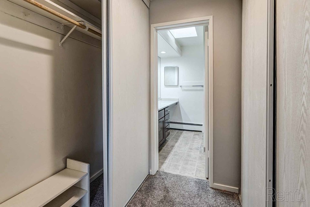 a hallway with a closet and a bathroom with a sink and a mirror