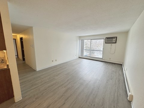 A spacious room with wooden flooring and a window overlooking a balcony.