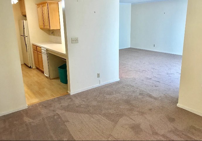 an empty living room with a kitchen in the background