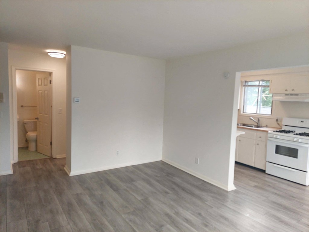 an empty living room and kitchen with white walls and wood flooring