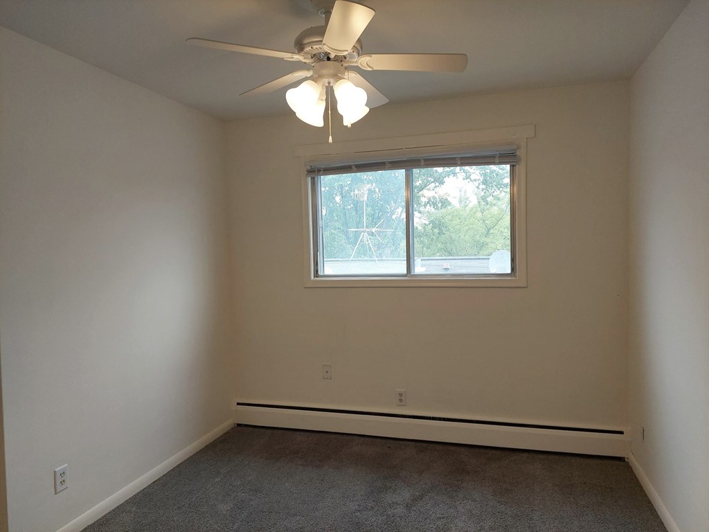 an empty bedroom with a ceiling fan and a window