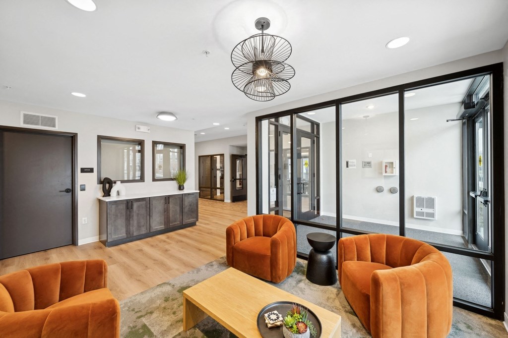 Wangstad Commons, Brooklyn Center,  A modern living room with orange chairs and a wooden coffee table.