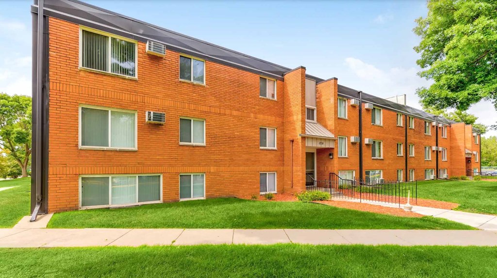 A red brick apartment building with green grass in front.