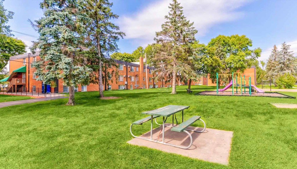 A green picnic table sits in a grassy area in front of a red building.